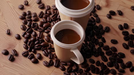 two coffee cups surrounded by roasted coffee beans on wood