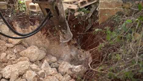 slow motion close up of an hydraulic hammer hitting and breaking a rock with material being blown away