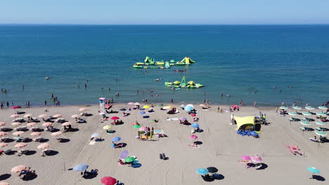 sand beach with umbrellas and people enjoying sunlight and swimming at the sea