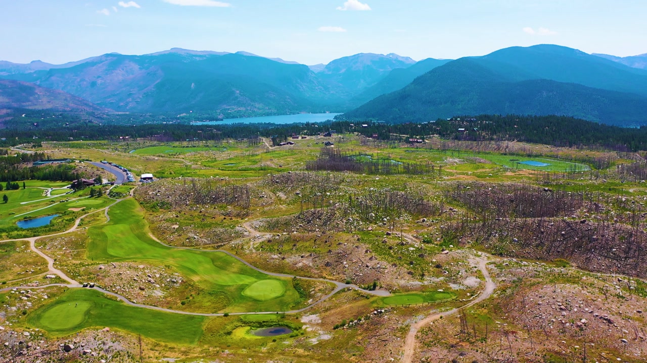 Drone panorama of bright golf fairways carved into a burned mountain landscape, with scorched trees, winding cart paths, and sweeping summer scenery near Rocky Mountain National Park Colorado.
