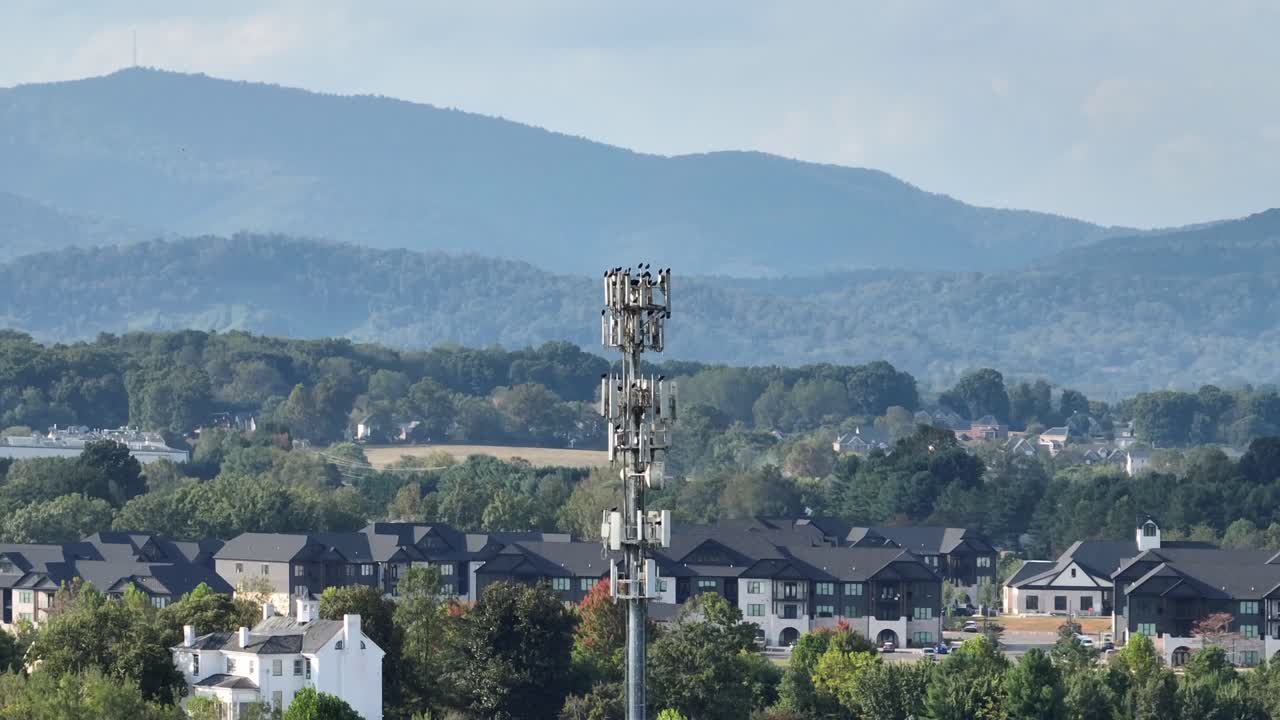 Aerial zoom orbit of tall cell tower rises above suburban homes with the Blue Ridge Mountains in the background. Modern infrastructure with scenic American nature in USA