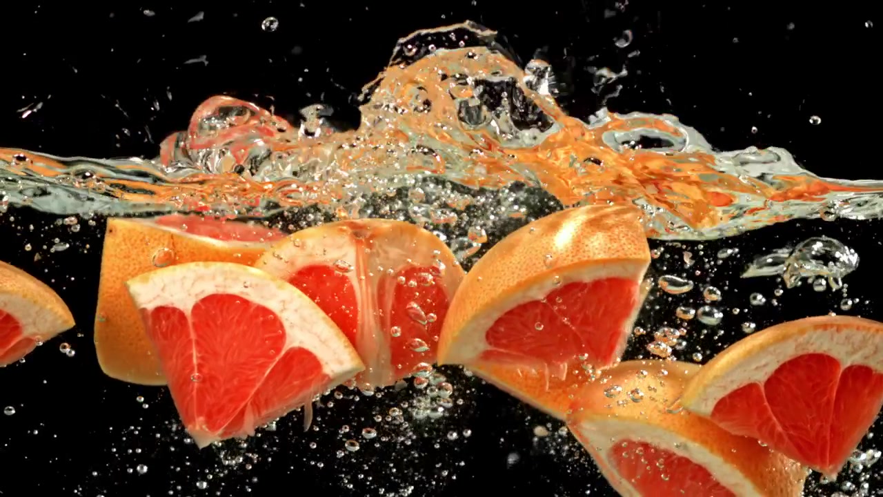 Friske grapefruktskiver plasker ned i vann i sakte film