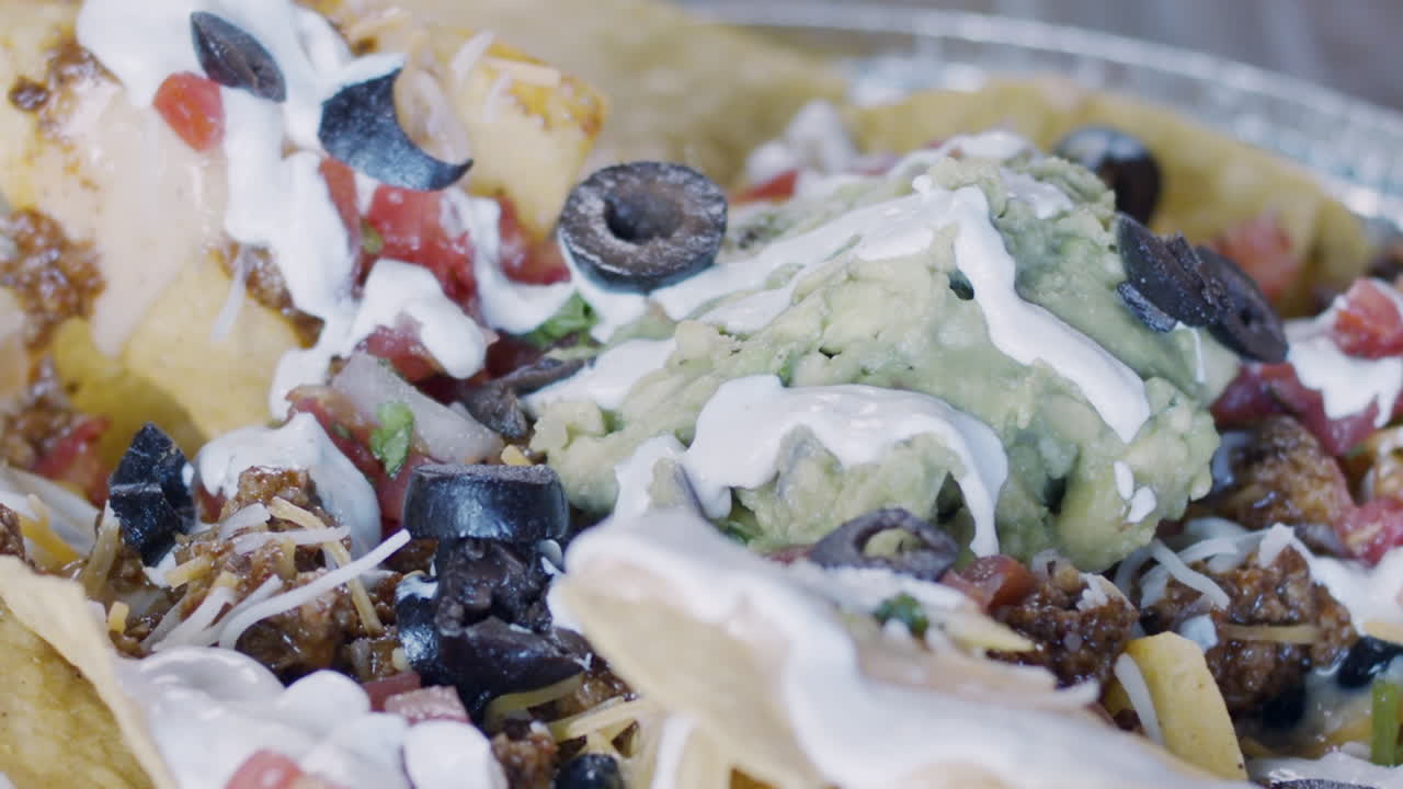 High speed shot of olives being dropped on loaded nachos