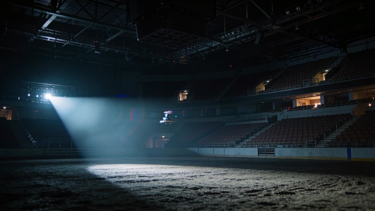 Attivazione del faretto sopraelevato, l'impianto di illuminazione proietta un cono di luce sul pavimento dell'arena, un drone si libra all'interno.
