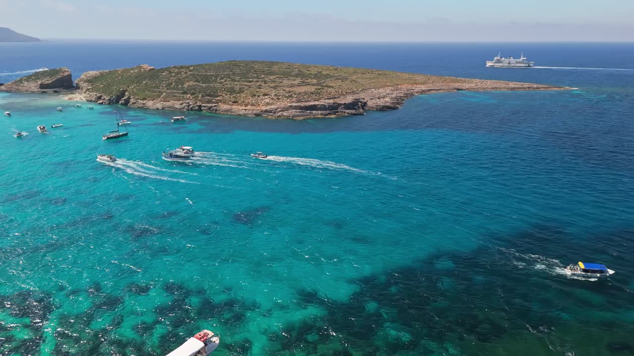 Laguna Blu, Comino, Malta, mostra barche e motoscafi in arrivo in acque mediterranee turchesi e cristalline vicino a coste rocciose e spiagge, vista dall'alto con drone in una giornata di sole.