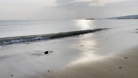 waves and sandy beach with sun reflecting on the surface