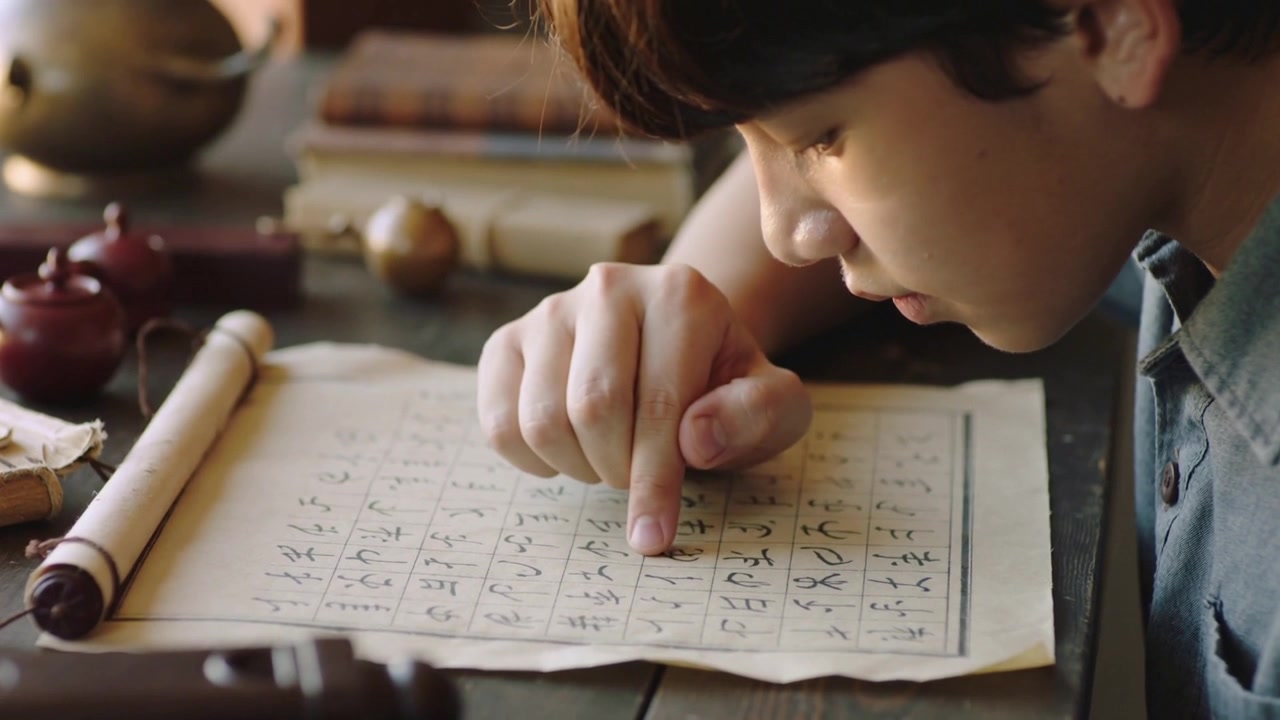 勉強机で身を乗り出し、子供が方眼紙に人差し指で文字をなぞりながら宿題をしている。