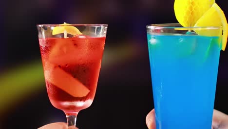 close-up of red and blue cocktails with lemon garnish in a vibrant setting.