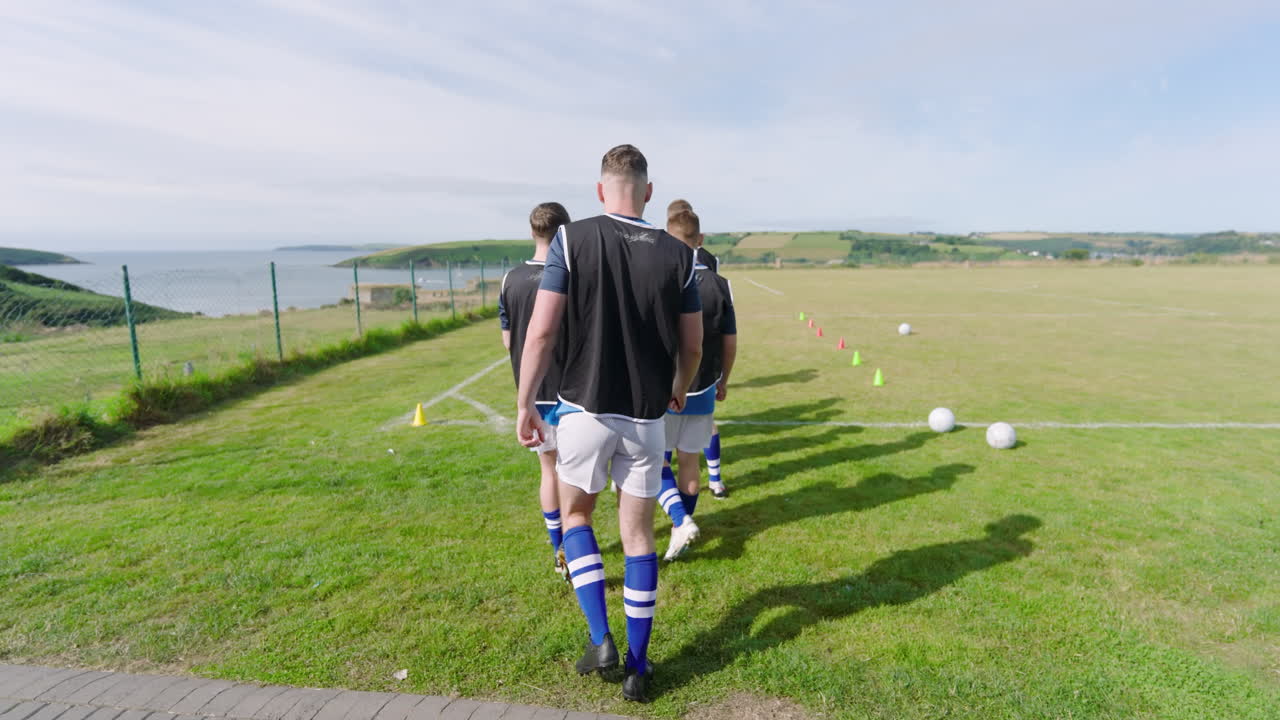 Male soccer players wearing black vests entering pitch and running with coach giving instructions