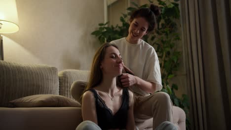 caring brunette woman brushing hair of her happy caucasian girlfriend