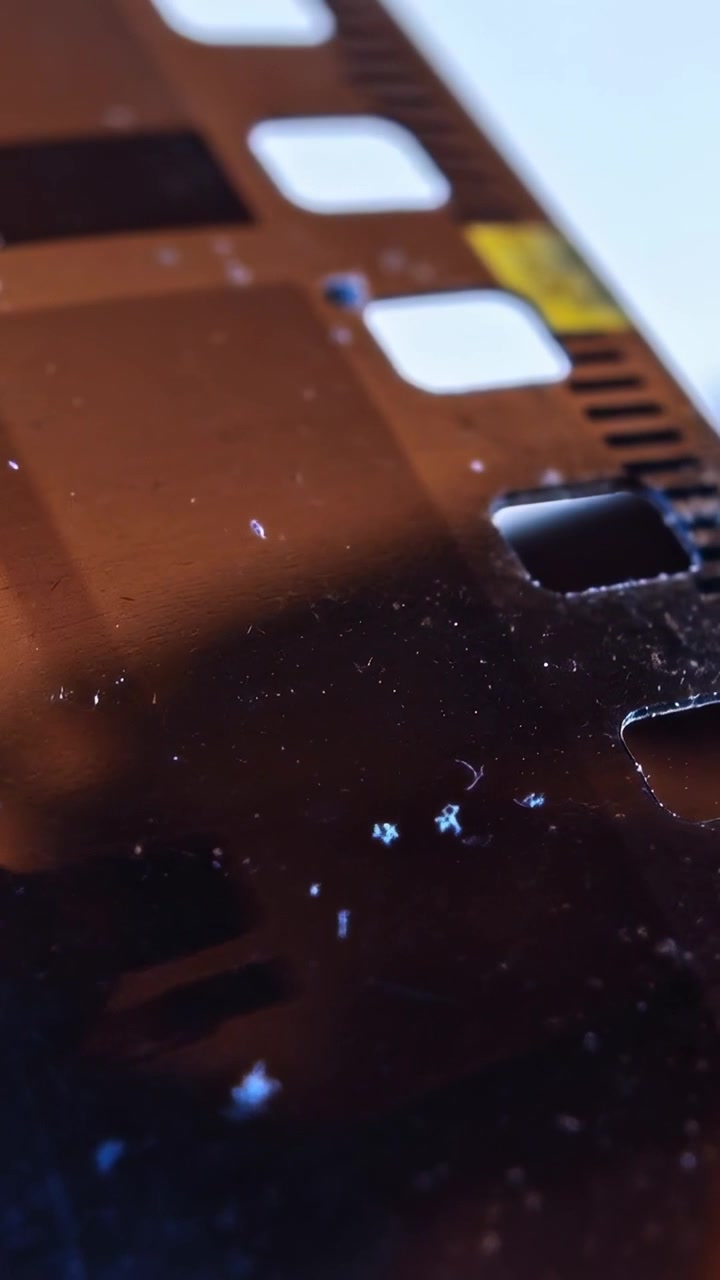 Video verticale: Striscia di pellicola inclinata che si sposta sul tavolo mentre la retroilluminazione aumenta, mostrando i fori di trascinamento.