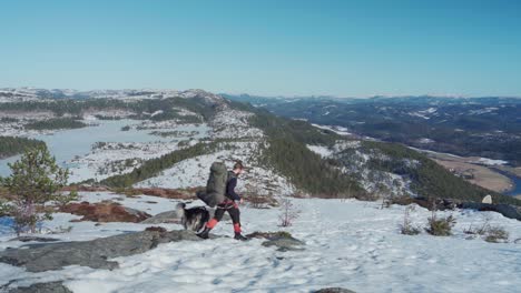 a man backpacker with his dog hiking in arctic mountain slope on winter sunny day in norway