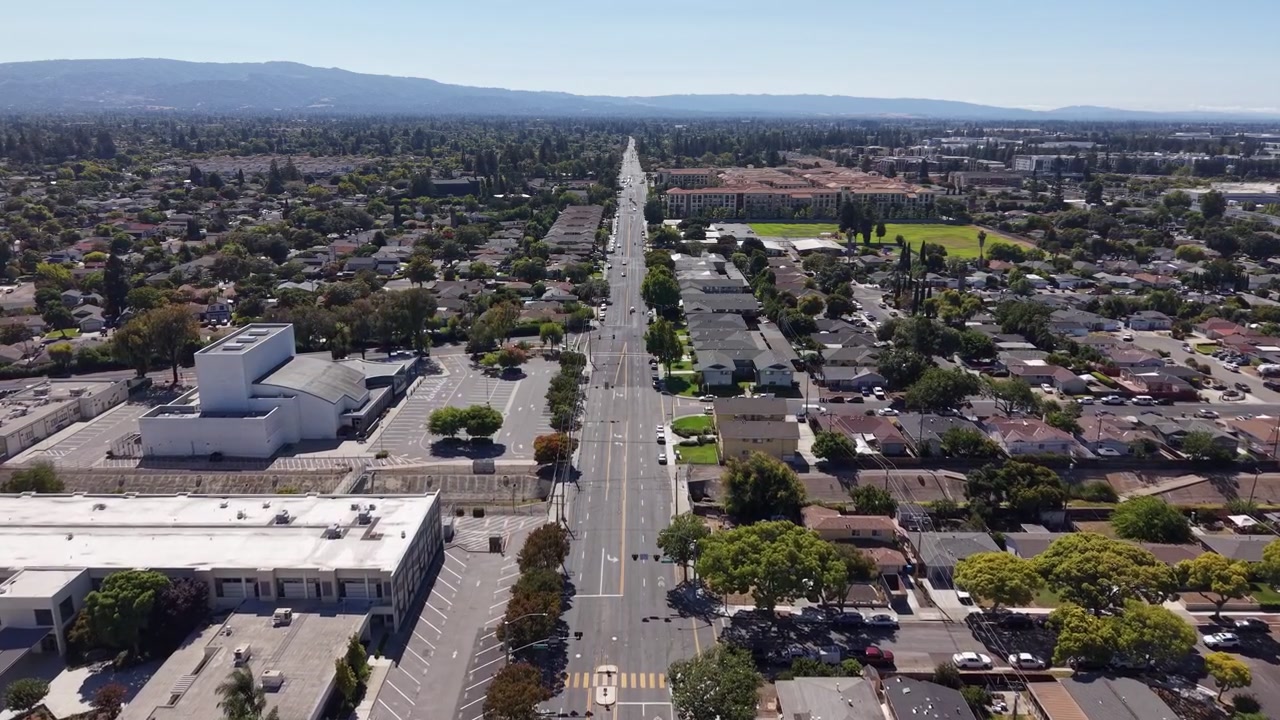 Veduta aerea dall'alto che percorre la lunga e dritta Monroe Street, mostrando il paesaggio suburbano di Santa Clara, California, con case residenziali ed edifici commerciali