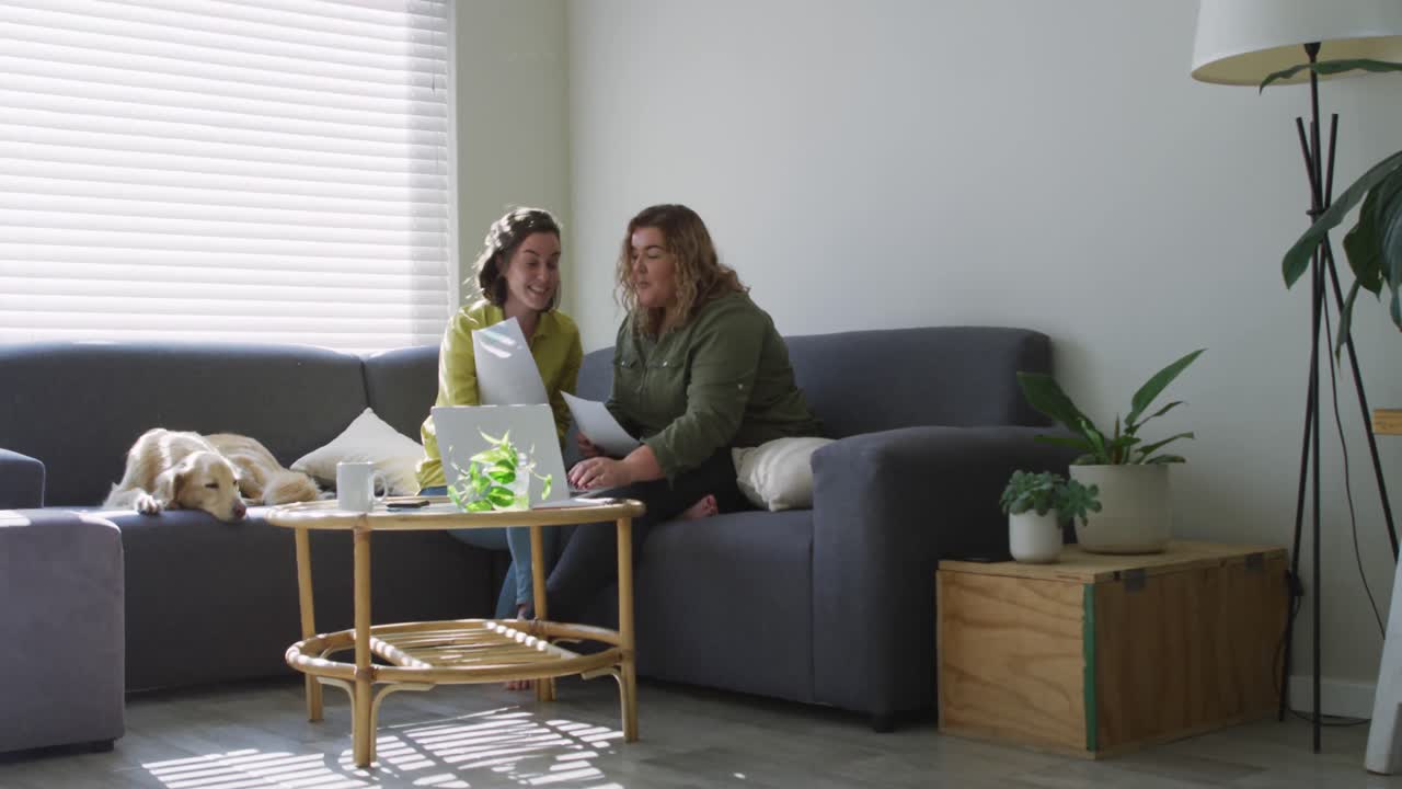 노란색 레즈비언 커플이 노트북을 사용하고 개와 함께 소파에 앉아 있습니다.