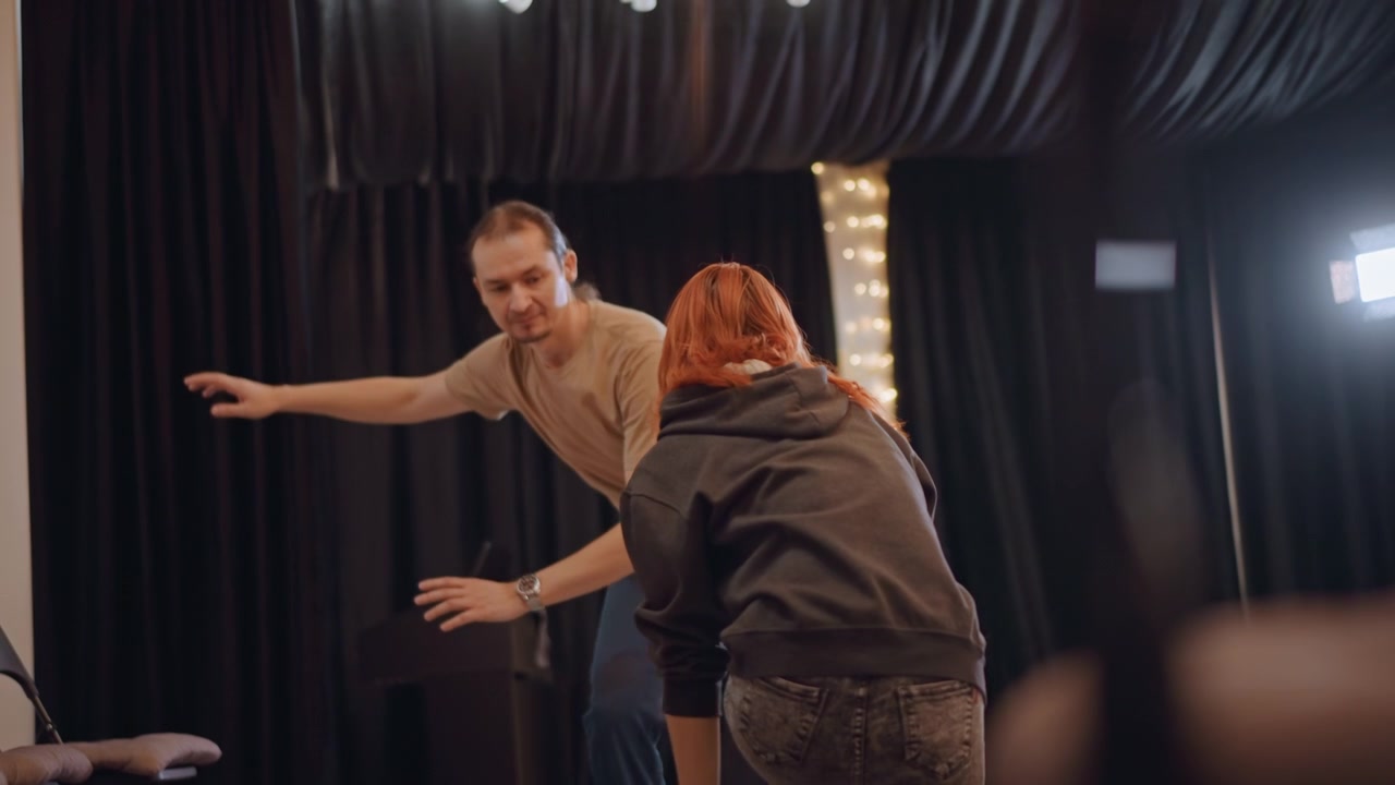 Dynamic improv scene in studio, redhead actor interacting with director through reach and response, stage lights and black curtains, playful tension, coaching cues and timing drills