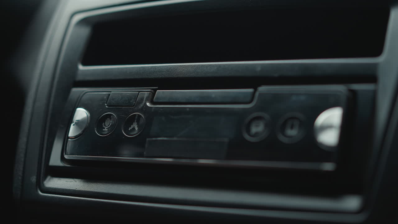 Male hands tap touchscreen to tune music on car console infotainment display with glowing icons and tactile buttons under soft cabin lighting highlighting dashboard trim and user interaction gesture