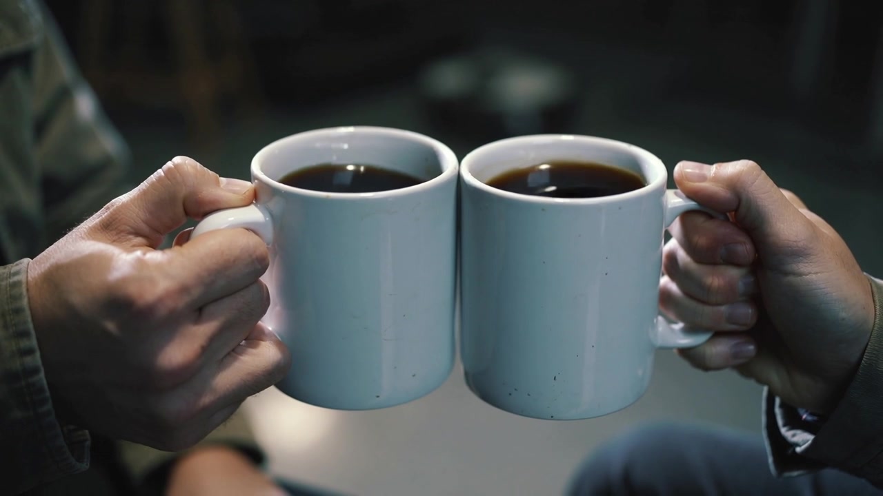 Due persone che fanno tintinnare tazze bianche in un salotto per una pausa caffè, mostrando una giacca verde.
