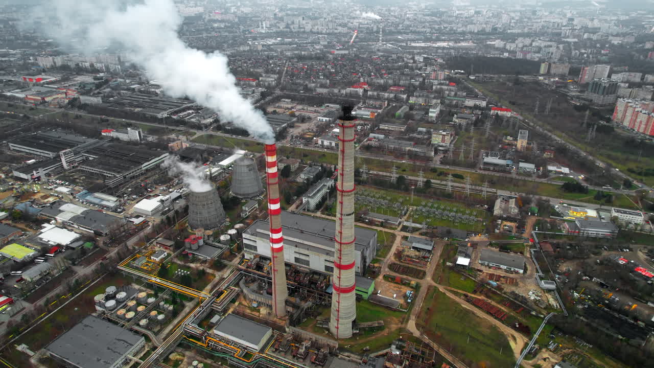 Aerial drone view of thermal power plant in Chisinau at cloudy weather, Moldova. View of pipes with felling steam, buildings and yellowed trees around
