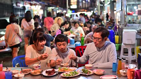 4k asian family eating food on street food restaurant at bangkok chinatown with traffic