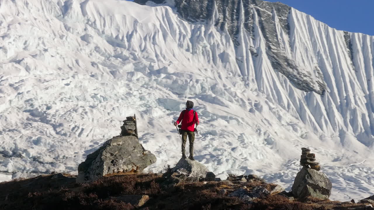 Ripresa aerea circolare con drone di un escursionista maschio presso un punto panoramico nella regione dell'Everest, in Nepal. La neve profonda copre le pendici delle montagne mentre una cresta innevata si estende sullo sfondo