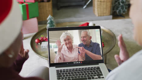 Diverse-senior-female-friends-using-laptop-for-christmas-video-call-with-happy-couple-on-screen