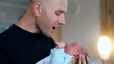 father holds his tiny newborn close to his face. man talks to his baby son waving him. close up. blurred backdrop.
