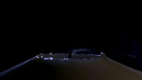 slow motion macro footage of a white candle lit by a match on a dark background
