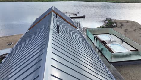 flying over the tin roof of a lakehouse revealing a boat dock on the lake and moody mountain terrain aerial dolly tilt