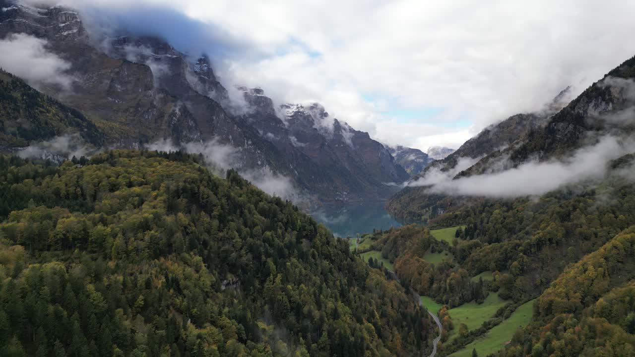 Zoom out shot of high mountain summits reaching the sky with dense tundra forest Kl&ouml;ntalersee Glarus Switzerland