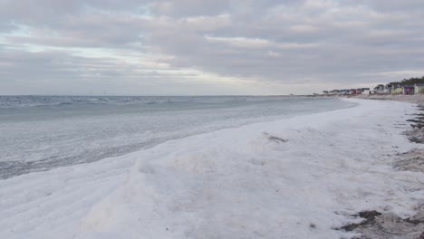 static shot of snowy beach and ice covered sea waves rolling in