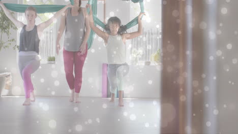 Animation-of-white-light-spots-over-diverse-female-instructor-and-teenage-girls-doing-aerial-yoga