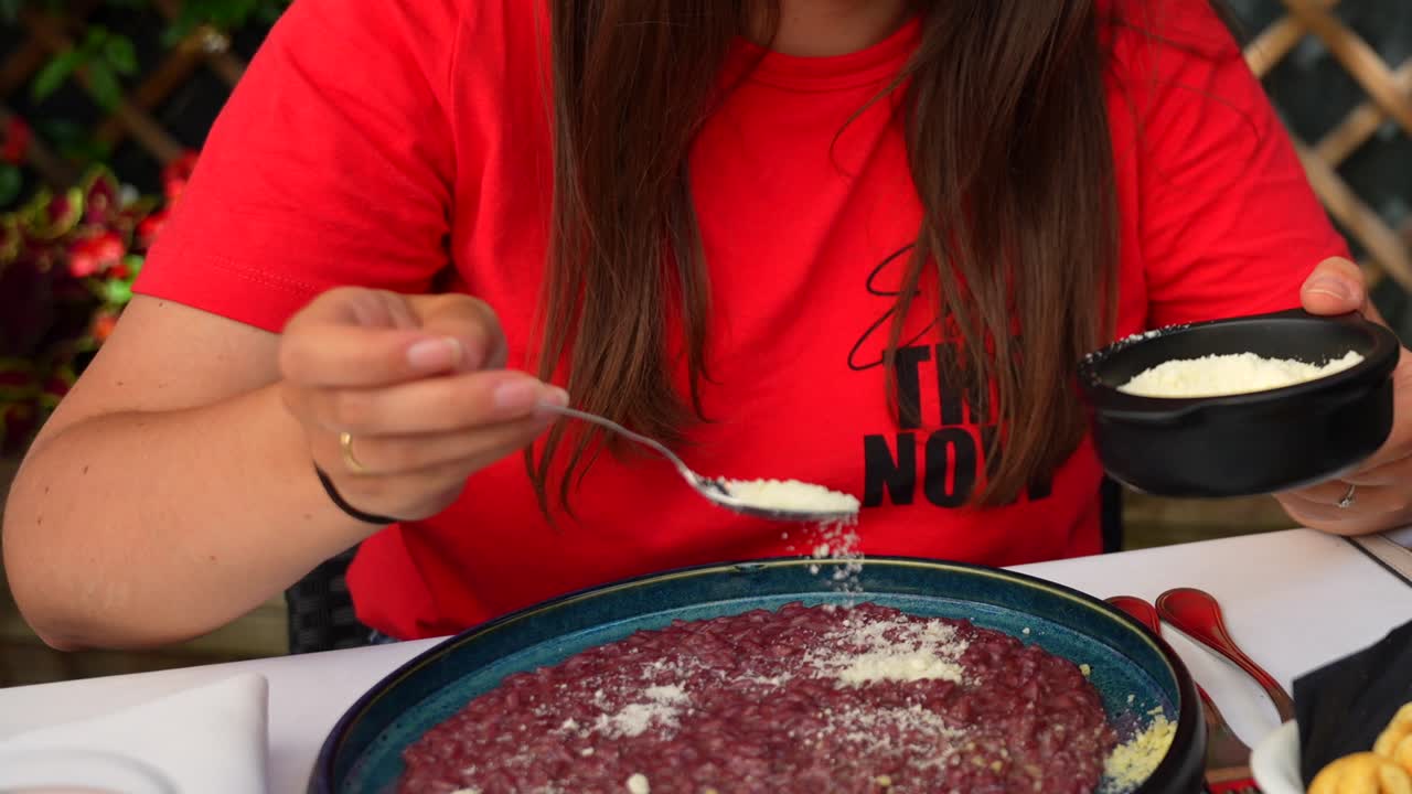 una mujer rociando polvo de queso en el risotto amarone de veronese.