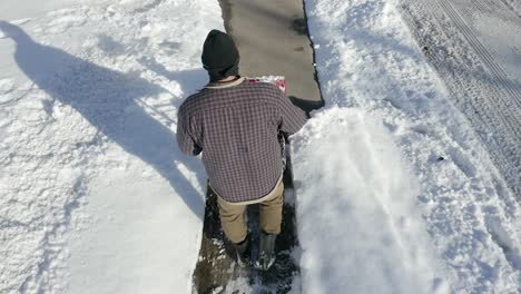 aerial view follows man down sidewalk using snow blower