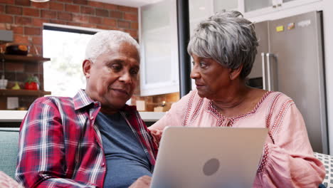 pareja mayor sentada en el sofá en casa usando una computadora portátil