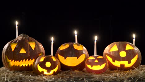 five halloween pumpkins with scary faces glow on black background