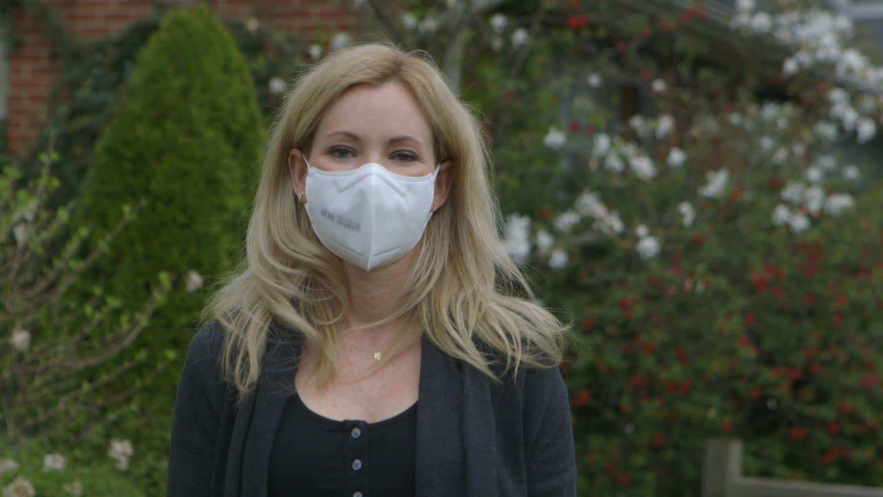 Attractive woman outside puts on a medical mask and looks into camera
