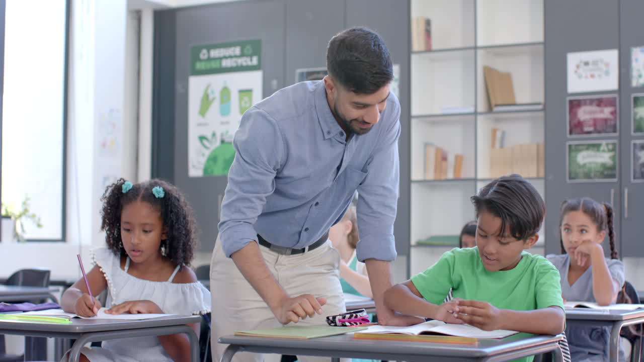 Teacher assists biracial boy and girl in a classroom at school