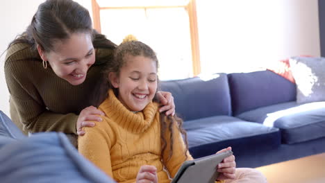 Glückliche-Biracial-Mutter-Und-Tochter-Sitzen-Auf-Dem-Sofa,-Mit-Tablet-Und-Lächeln-Im-Sonnigen-Wohnzimmer