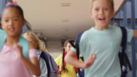 Front-view-of-mixed-race-schoolkids-with-schoolbags-running-in-the-corridor-at-school-4k