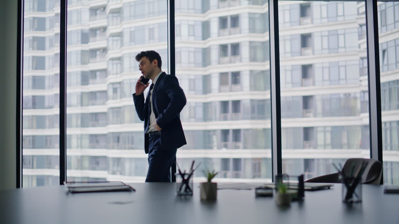 Elegant manager negotiating smartphone by office window. Businessman calling