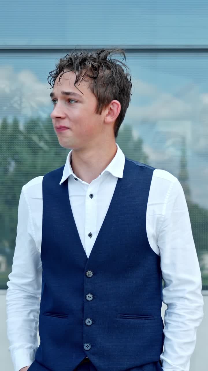 A vertical close-up shot shows a young man in formal business attire standing outdoors, appearing thoughtful and slightly concerned