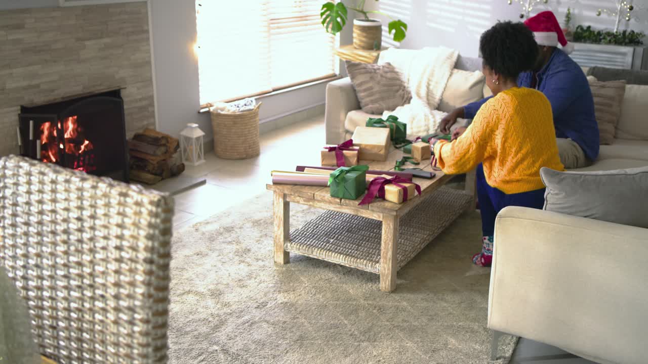 Gathering supplies, African American couple wrapping presents on coffee table for holiday season