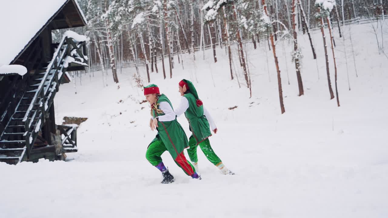 Two fabulous elves in green suits ran into the hut to warm themselves after they had frozen outside. Winter landscape. Slow motion