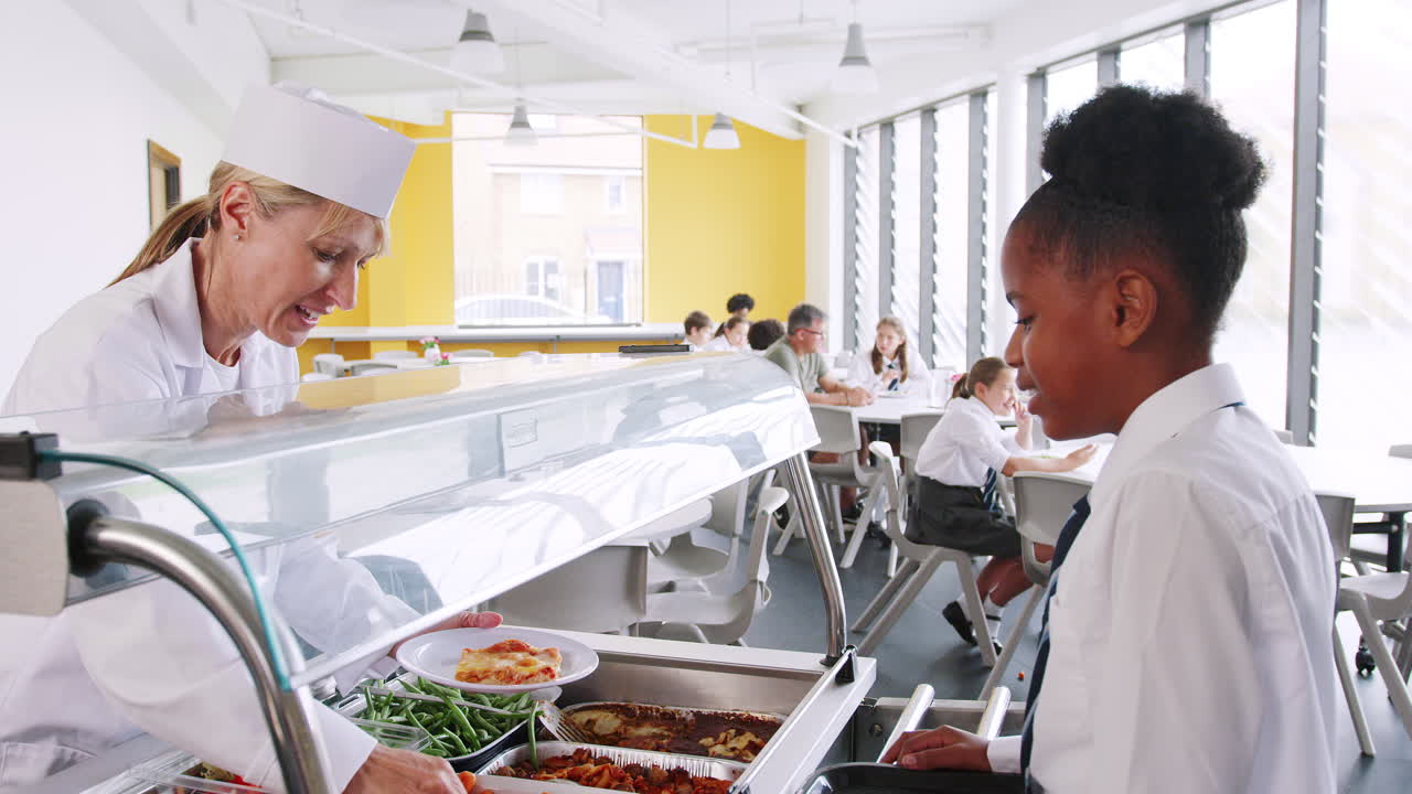 유니폼을 입은 여자 고등학교 학생이 식당에서 음식을 제공 받고 있습니다.
