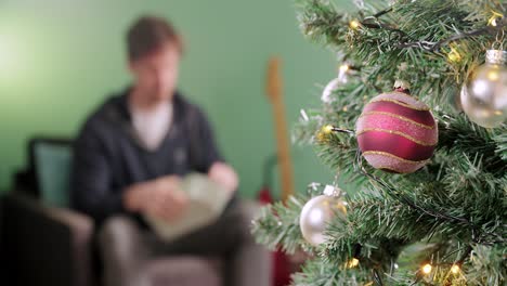 el hombre está emocionado al desenvolver un regalo en la mañana de navidad con un árbol de navidad en primer plano