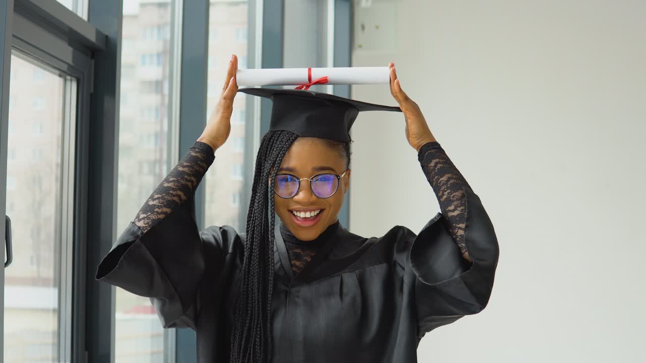 una graduada alegre sostiene un diploma sobre su cabeza y posa para la cámara. mujer afroamericana con educación superior