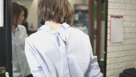 Woman-coming-to-the-barber's-chair-and-sitting-down-in-front-of-a-mirror-in-the-Beauty-Salon,-waiting-for-her-hairdresser-to