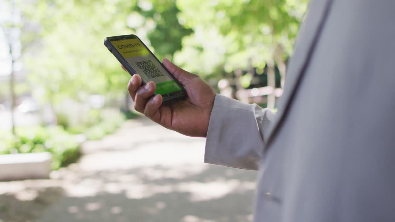 도시에서 코로나바이러스 여권을 가진 스마트폰을 사용하는 아프리카계 미국인 남자의 손