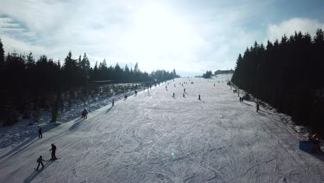 Aerial-panoramic-view-of-Topolita-Snow-summit-with-people-snoboarding-and-skiing-down-slope-while-drone-flies-uphill