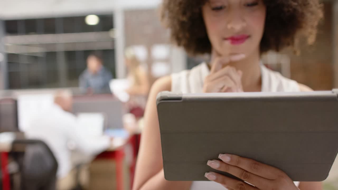 retrato de feliz mulher de negócios criativa biracial usando tablet em escritório casual, em câmera lenta